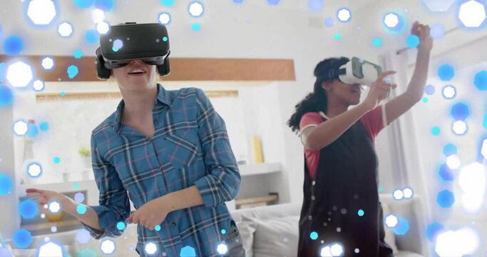 Animation of blue and white spots over two happy diverse teenage girls in dancing in vr headsets
