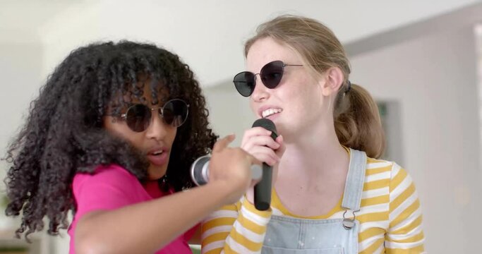 Animation of lights over happy diverse teenage girls with sunglasses and microphones singing at home