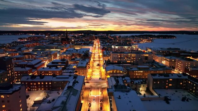Snow-covered cityscape at dusk with illuminated streets, aerial view