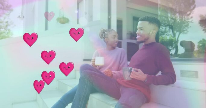 Animation of hearts over happy diverse couple drinking tea at home
