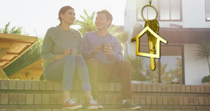Animation of gold house key and key fob over diverse couple drinking tea at new home
