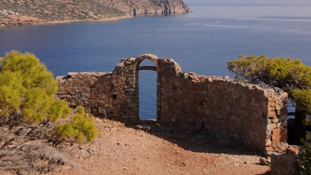 Old archway entrance ruins looks over stunning blue bay on island of Spinalogka Crete Greece