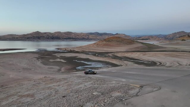 black pick truck driving along a dried lake bed at dusk with his lights on in Millerton Lake Fresno California 60fps