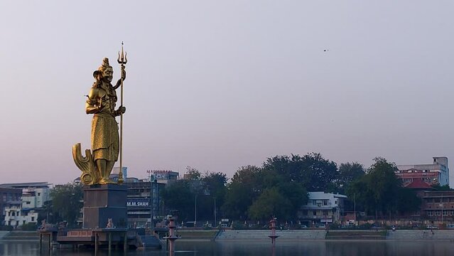 Enjoy a beautiful side view of the immense gilded Lord Shiva statue in Sursagar Lake, Vadodara, as dusk settles, creating a serene and enchanting atmosphere.