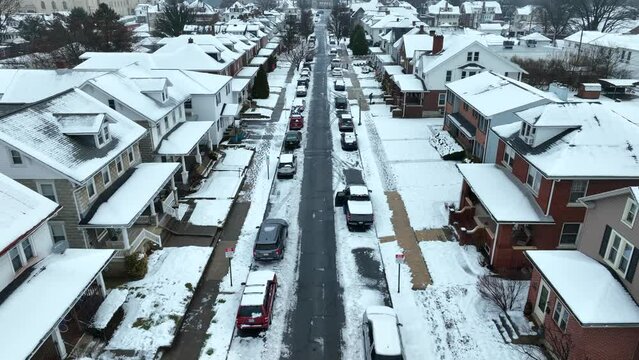 Parking cars in narrow street of american neighborhood. Snowy roofs of homes and buildings in winter. Aerial birds eye backwards shot.