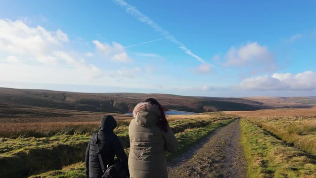 Young boy and his mother walking on a rural footpath on a day out in the country. Countryside activity scene with moorlands and a large lake