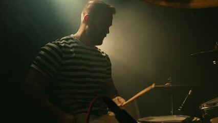 Male drummer emotionally plays a drum kit in a dark room full of smoke. Music band rehearsal. Music or song recording, creation