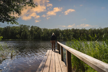 Athletic girl on a wooden pier on a forest lake in Estonia on a summer evening, photo from the back.