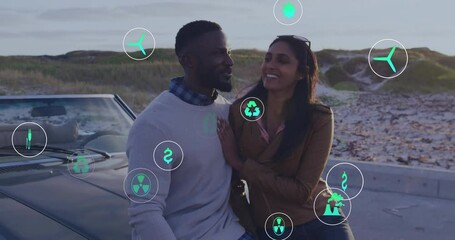 Animation of ecology icons over happy diverse couple on road trip embracing by car - Powered by Adobe