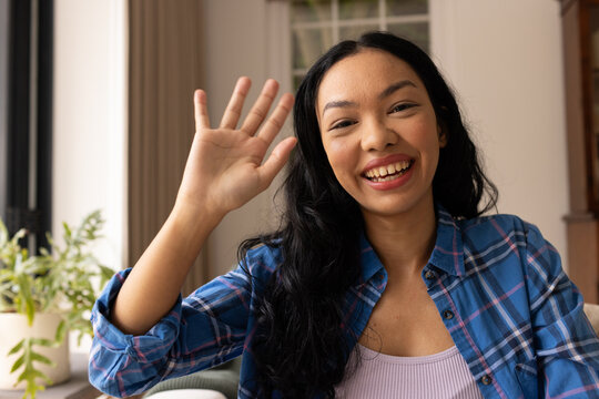 Young biracial woman waves at the camera from home on video call