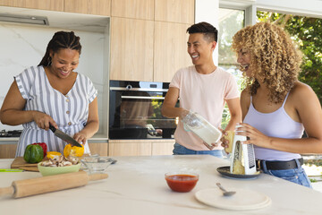 Young Asian man and two young biracial women enjoy cooking together at home