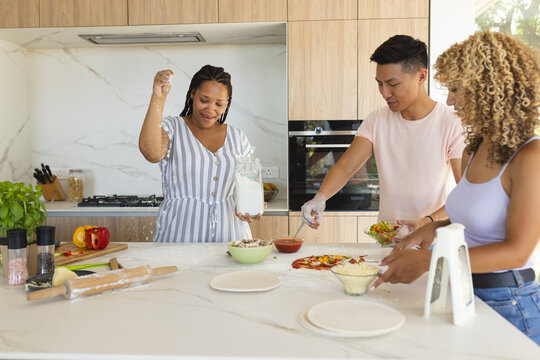 Young Asian man and biracial women cooking together in a modern home kitchen and making pizza