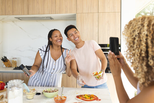 Young Asian man and young biracial woman pose for a photo in a home kitchen, making pizza