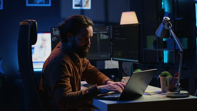Computer scientist putting headphones on while developing code on PC, making time pass faster during remote job shift. IT admin doing multitasking in home office while listening music, camera A
