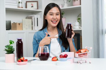 Smiling young beautiful Asian reviewing tasty mixed strawberry and cherry juice detox drinks,...