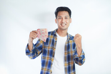 Adult Asian man clenched fist while holding Indonesia paper money and showing excited expression