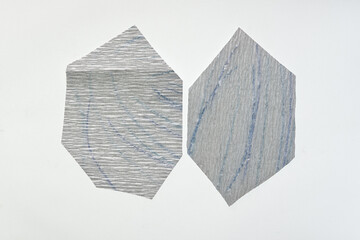two irregular hexagonal metallic silver crepe paper shapes on a blank surface