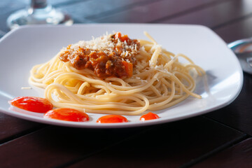 spaghetti bolognese with cheese sprinkled is placed on a white plate with a wooden background