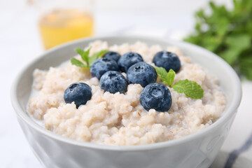 Delicious barley porridge with blueberries and mint in bowl on white table, closeup