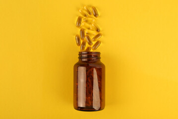 Glass medical bottle and vitamin capsules on yellow background, top view