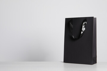 Black paper bag on white wooden table, space for text