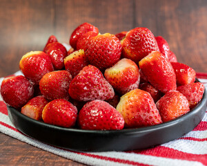 Frozen strawberries on a black plate with wooden background. Close-up.