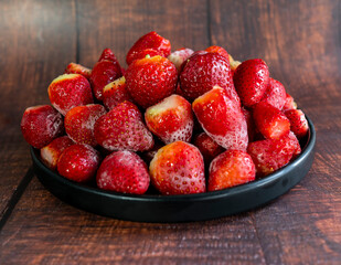 Close-up of frozen strawberries on a black plate, with wooden background.