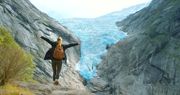 Glacier, open arms or woman hiking on mountains travel adventure to explore on holiday vacation. Traveller, outdoor or back of hiker trekking with fresh air for freedom, nature or gratitude in Norway
