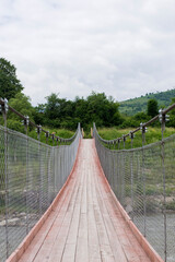 Obraz premium A new wooden bridge over a mountain river on cables. Ukrainian Carpathian Mountains. A bridge over a mountain river. Green grass and trees.
