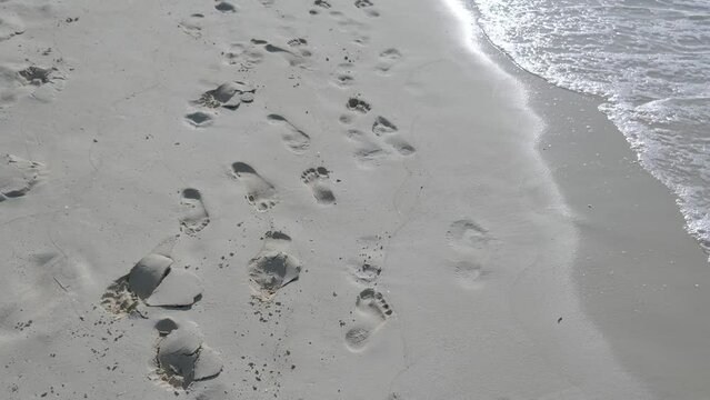 Footprints on the beach in sand with ocean waves flowing in