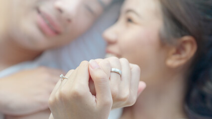 Top view young couple asia people lying down talk on bed relax smile hold hands look at ring on...