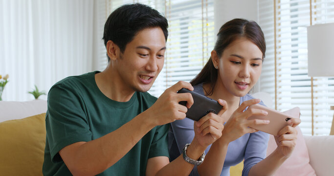 Young adult asia cute sweet couple enjoy playing sport match game online in esport race lover at home sofa couch. Two Gen Z people man and woman gamer happy relax smile laugh joy fun video gaming app.