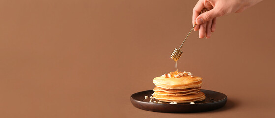 Hand with honey dipper and stack of tasty pumpkin pancakes against beige background with space for text