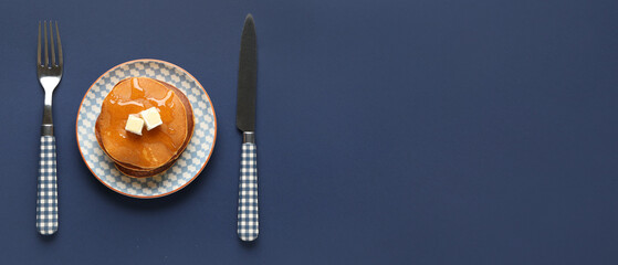 Plate with tasty pumpkin pancakes, knife and fork on blue background with space for text