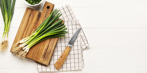 Cutting board with green onion and knife on white wooden background with space for text