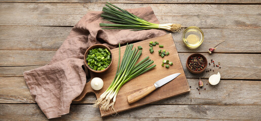 Cutting board with green onion, knife, oil and spices on wooden background