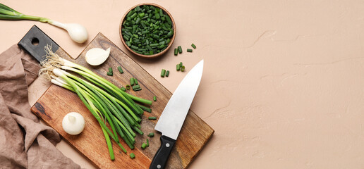 Cutting board with green onion and knife on beige background with space for text
