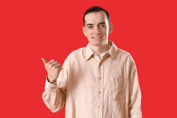 Young man pointing at something on red background