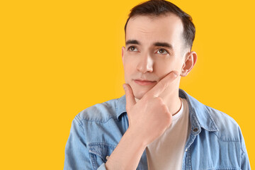 Thoughtful young man on yellow background, closeup
