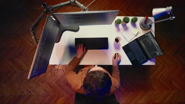 Top down view of remote worker typing code in personal office, using javascript language to develop software application. It specialist using multimonitor desktop setup to finish project, aerial shot