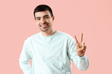 Naklejka premium Young man showing victory gesture on pink background