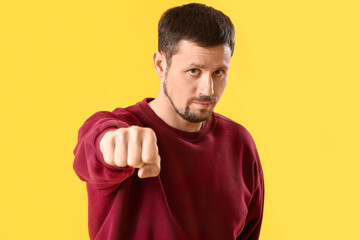 Handsome man with clenched fist on yellow background, closeup