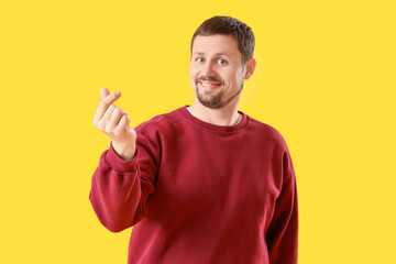 Handsome man making heart gesture on yellow background