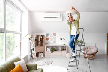 Young man standing on ladder and changing light bulb in lamp at home