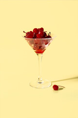 Glass of tasty maraschino cherries on yellow background