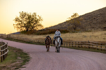 Cowgirl riding grey quarter ranch horse leading a horse in the fall
