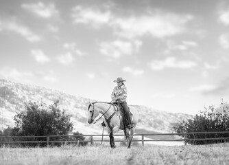 Cowgirl riding grey quarter ranch horse in the fall
