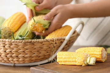 Woman peeling fresh corn cob on wooden table