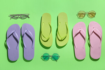Fototapeta premium Colorful pairs of flip flops and sunglasses on green background
