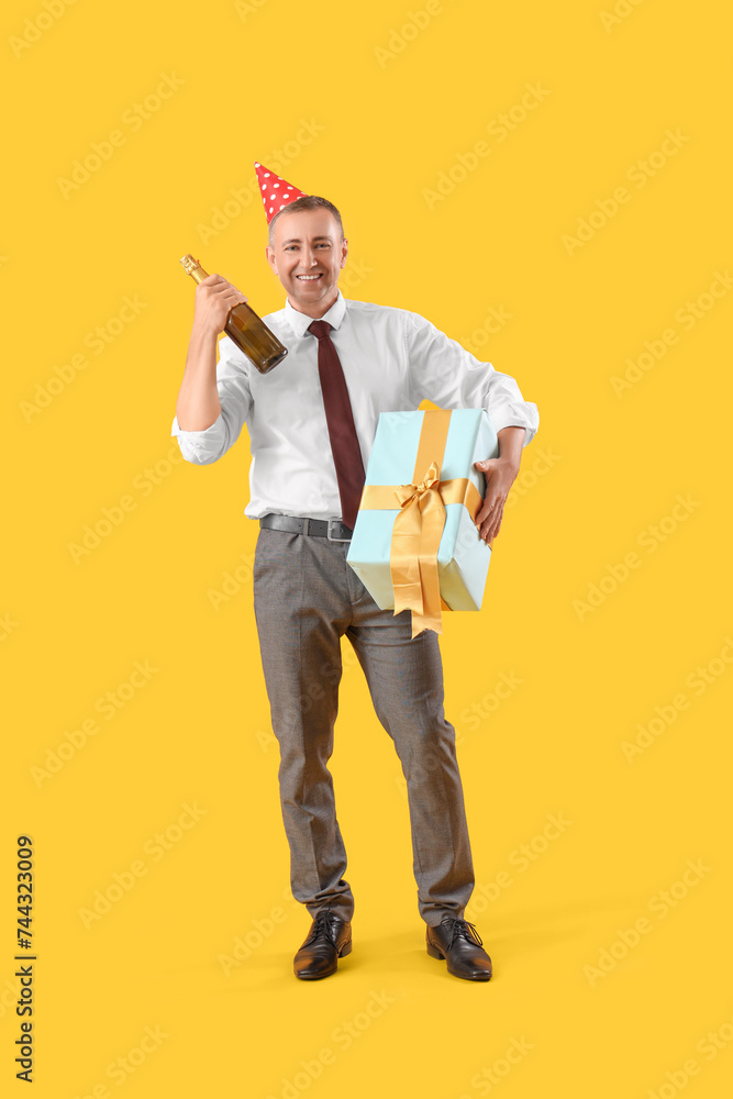 Poster mature businessman with birthday gift and champagne on orange background